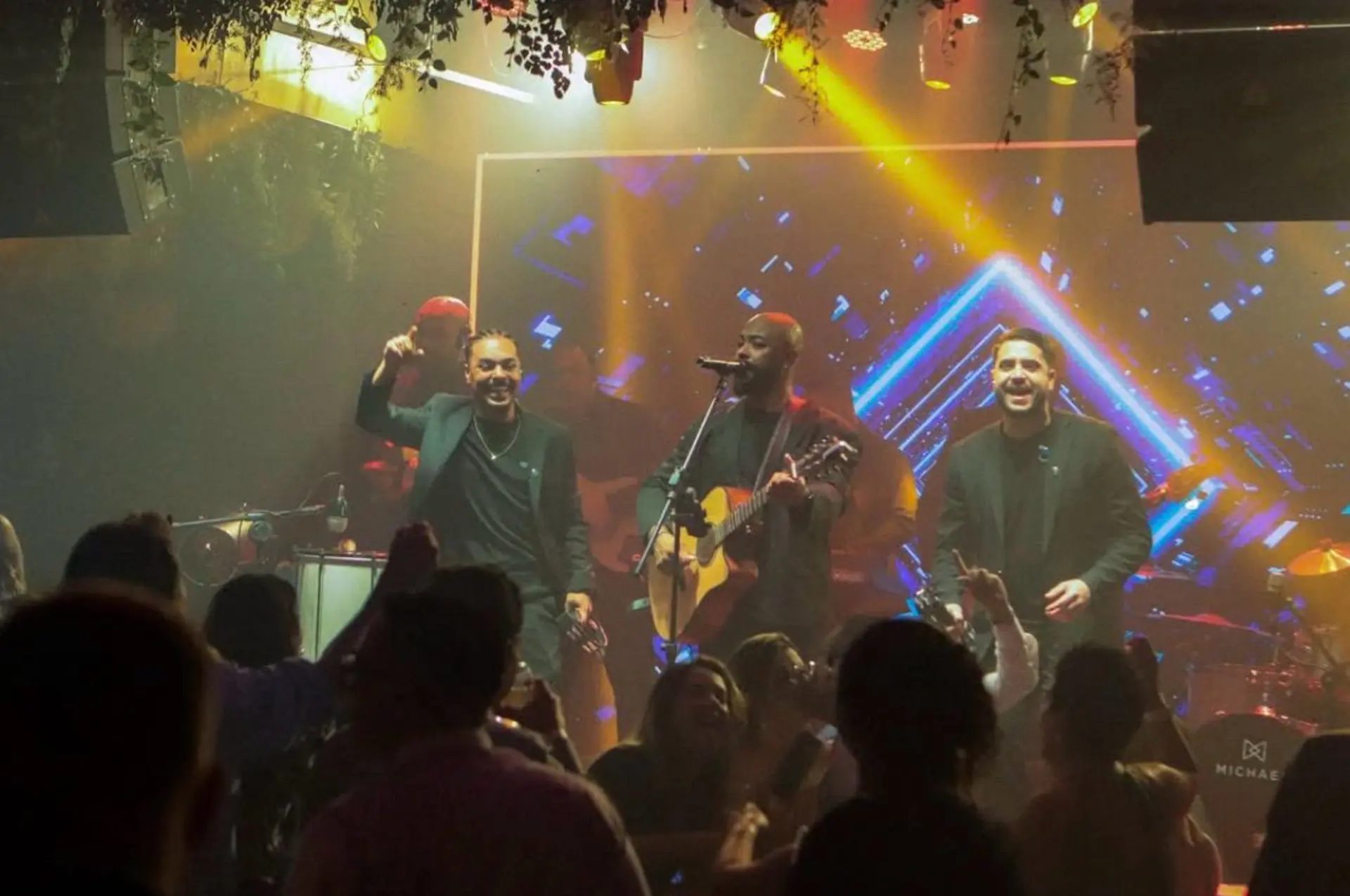 Trio se apresentando em meio ao público em ambiente de casa noturna