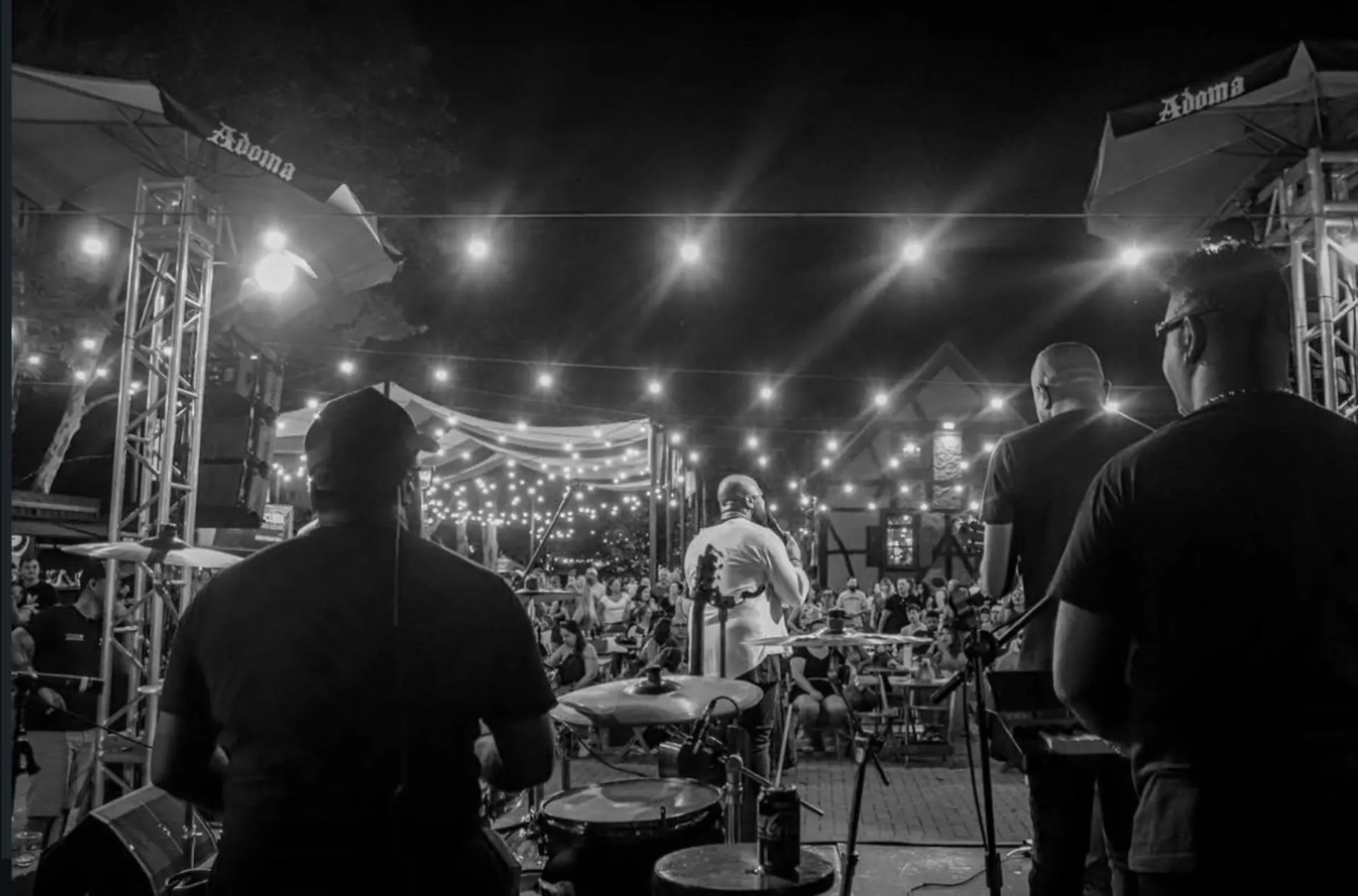 Banda vista de trás com público ao fundo, em preto e branco